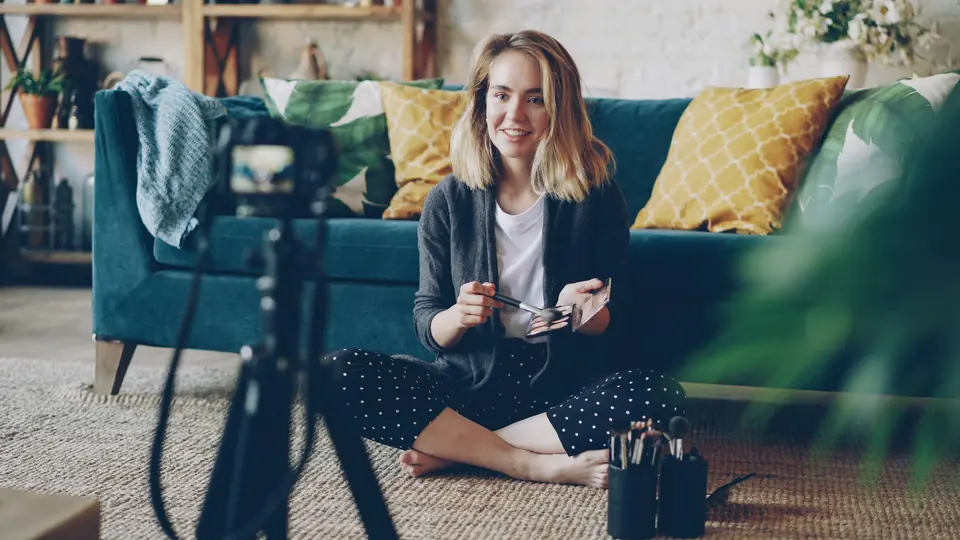 A creator sitting on a living room floor, talking to a camera on a tripod